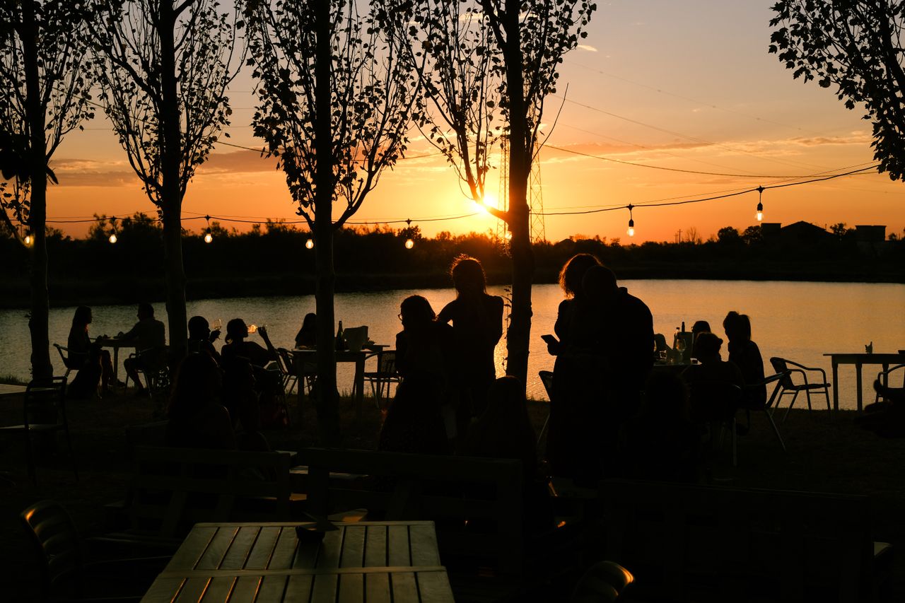 about-01 People silhouetted against a sunset by a lake, creating a serene outdoor party ambiance.