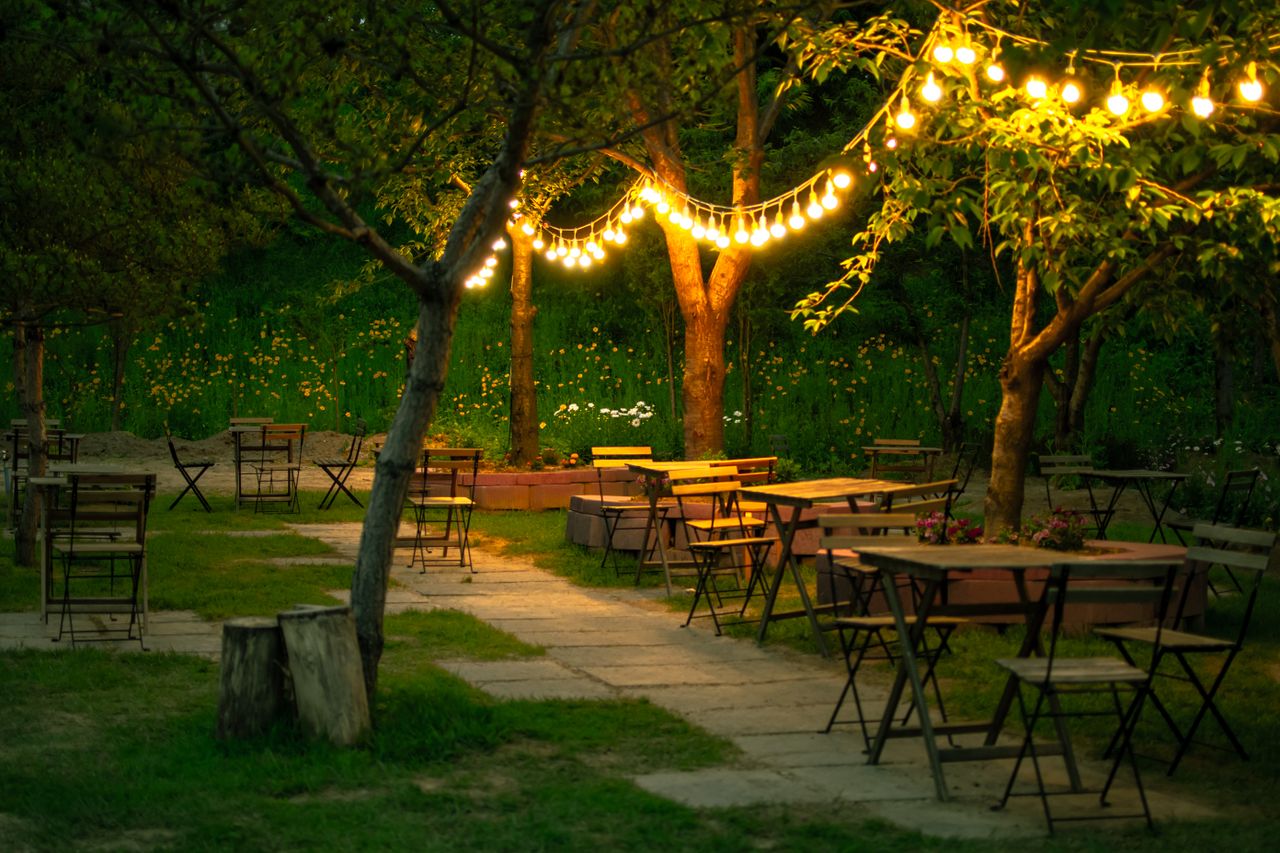 hero-img-02 Cozy outdoor restaurant with wooden tables and charming string lights in a garden setting.