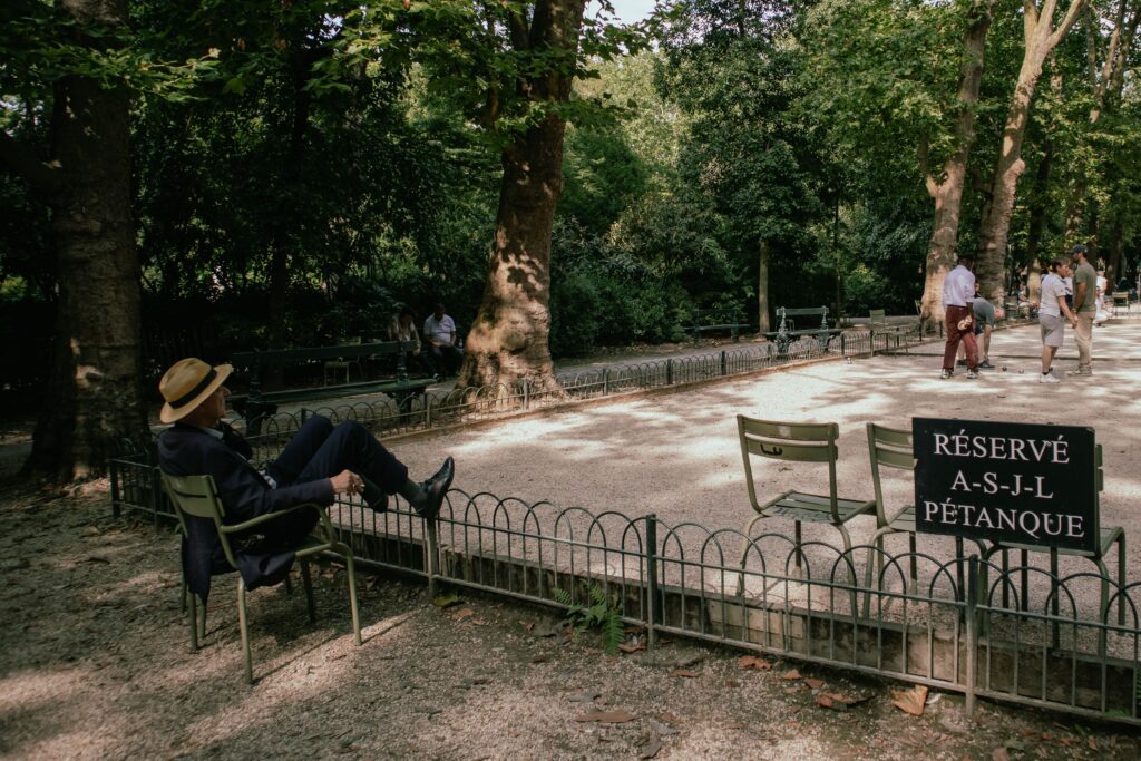 pexels photo 32431779 32431779 A serene park scene in Paris with a man relaxing, people playing pétanque.